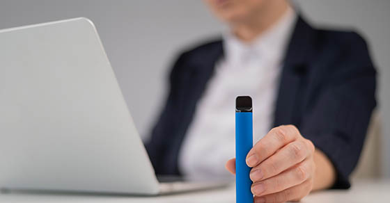 Background of an employee at their desk with a vaping device in the foreground